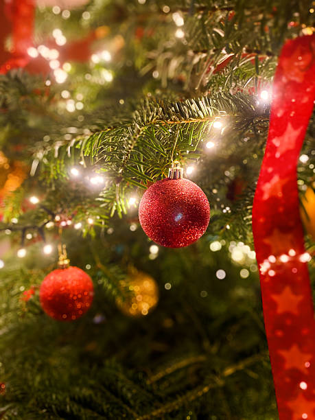 A close-up shows part of a Christmas tree decorated with sparkly red and gold balls. A red ribbon with stars adds more color, and the bright lights twinkle, evoking a sense of magic and wonder. Christmas, Christmas Eve