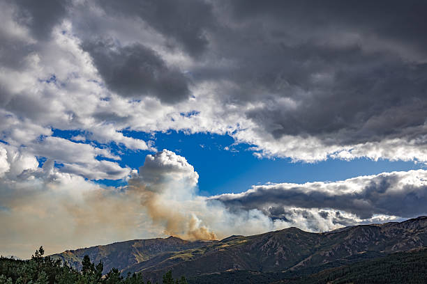 Sierra Norte de Guadalajara Natural Park. Guadalajara province. Spain. Wildfire burning on a forested mountain landscape under a partly cloudy sky, showing smoke plumes rising into the air