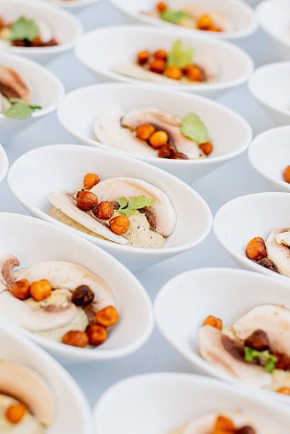 Close-up of elegant catering mini bowls with sliced mushrooms, roasted chickpeas and garnish, served at an event.