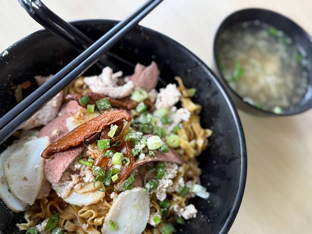 A bowl of Chinese MeePok aka flat yellow noodle Served with minced pork meat, braised mushrooms, fish cakes and scallions