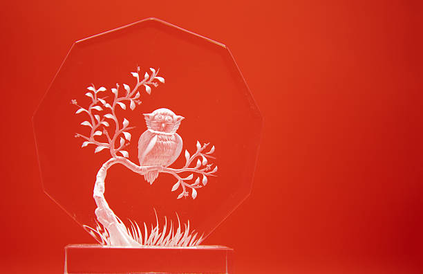 Decorative glass ornament featuring an etched owl perched on a branch, displayed against a red background.