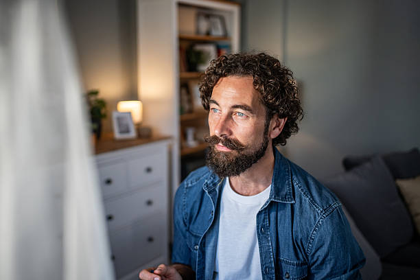 istock Man contemplating at home with beard and curly hair 2237680974