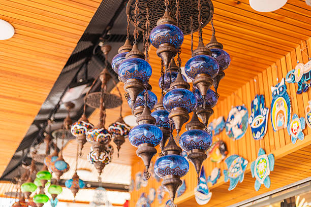 Beautifully crafted blue glass lanterns dangle from the ceiling in a lively market. Surrounding them are unique artworks and crafts, creating an inviting atmosphere