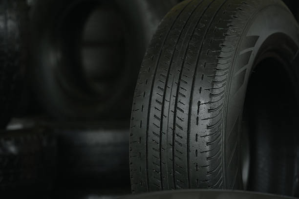 Three stacks of slick racing tires stand on asphalt near a truck or trailer, suggesting a motorsport setting for the worn rubber