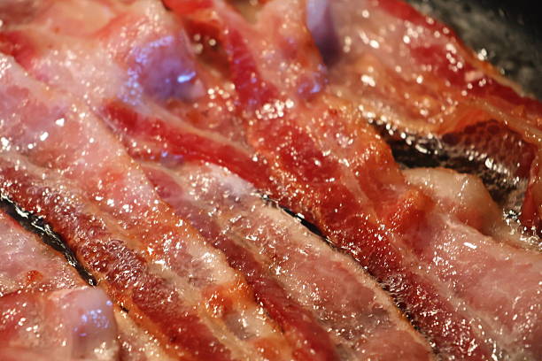 Multiple slices juicy bacon sizzling on the frying pan.