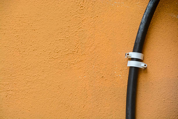 a black pipe and white clips against a textured orange wall, creating a visually appealing interplay of color, line, and surface detail.