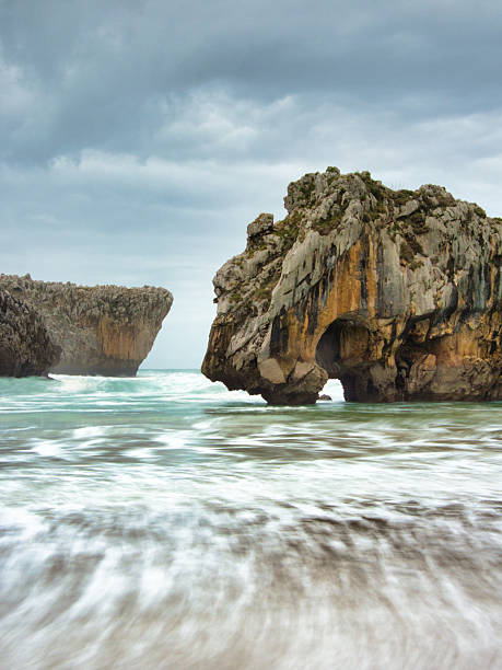istock Hidden Beach and Jagged Sea Caves - Secluded beach between imposing limestone cliffs with sea caves and crashing waves on a dramatic, overcast day in Asturias, Spain. 2237702134