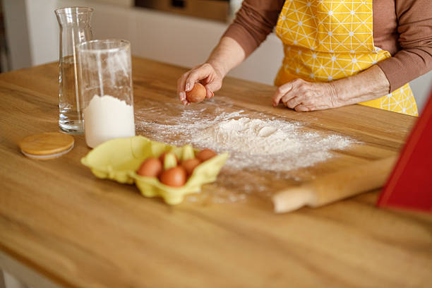istock Midsection of senior woman cracking eggs into flour on kitchen island while preparing cookies at home 2237706860