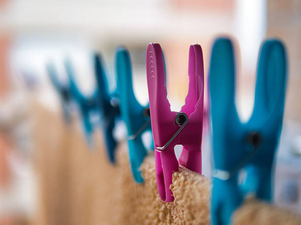 Pink Clothespin Focus Blue Line Blur - Bright pink and blue plastic clothespins gripping a towel on a clothesline. Shallow depth of field for a fresh laundry and chore concept.