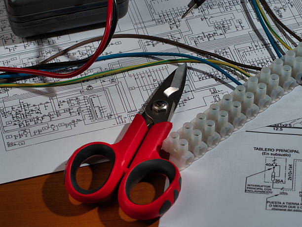 Electronic Work Multimeter Wires Zenith View - Top-down view of a multimeter, terminal block, snips, and wires on complex electronic schematics. Represents electrical engineering, installation, repair, and technology.