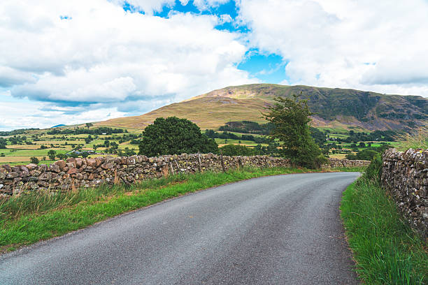 Country road curving through the rural lake district countryside with stone walls and hills