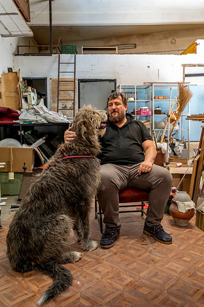 istock Man sitting and petting a large irish wolfhound in an cluttered old workshop 2237719231