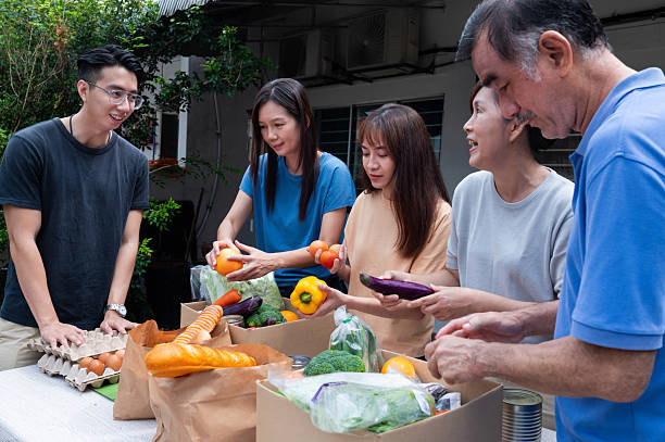 istock Volunteers from a mixed age group pack cardboard boxes with free meals and distributing them to struggling families at a vibrant outdoor charity food drive 2237723255