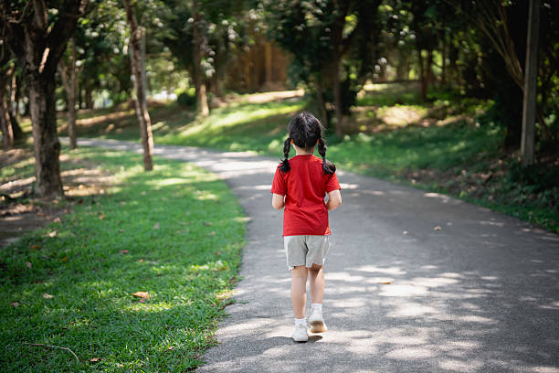 istock Young child walking through a serene park path surrounded by trees, enjoying a peaceful moment in nature on a bright sunny day 2237731488