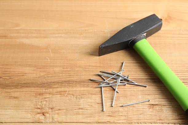 Closeup of a man's hand holding a generic, mass produced hammer against a wood background.