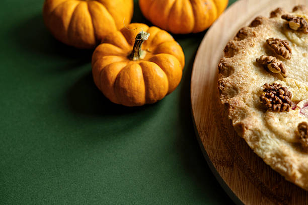 Homemade pie with walnuts and apple on a wooden board, styled with mini pumpkins on dark green background. Copy space.