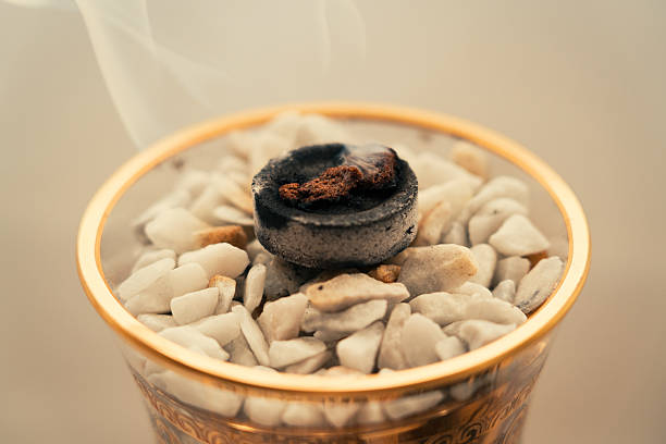 A close-up view of a traditional incense burner basket with white stones and\nbukhoor creating smoke, focusing on Middle Eastern culture and scent.