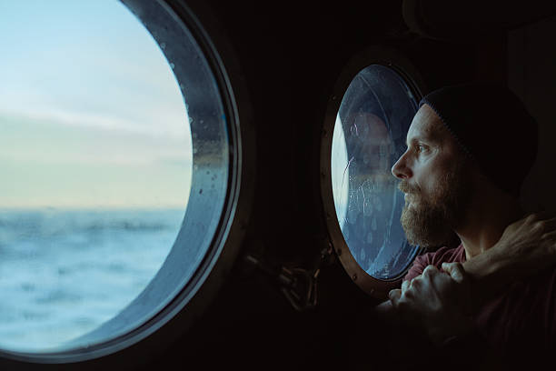 Traveler gazing at the open sea through a ship porthole, thoughtful moment during a maritime journey.
