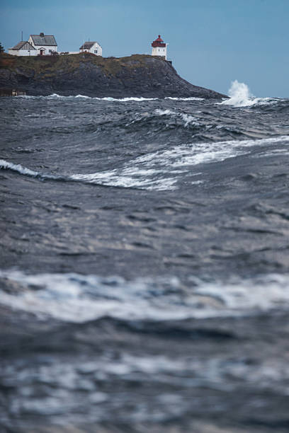 View of a lighthouse and houses on a rocky coastal cliff, overlooking stormy waves of the North Atlantic. The scene highlights navigation, safety, and the dramatic nature of northern seas.