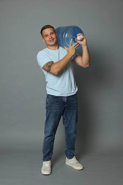 istock Smiling delivery man with cooler bottle of water on grey background 2237762677