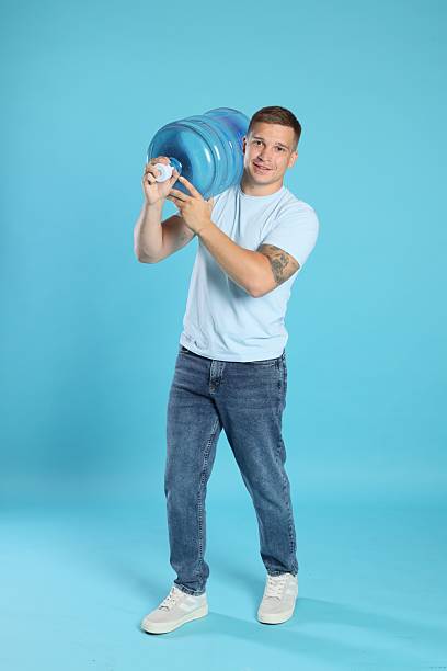 istock Smiling delivery man with cooler bottle of water on light blue background 2237762690