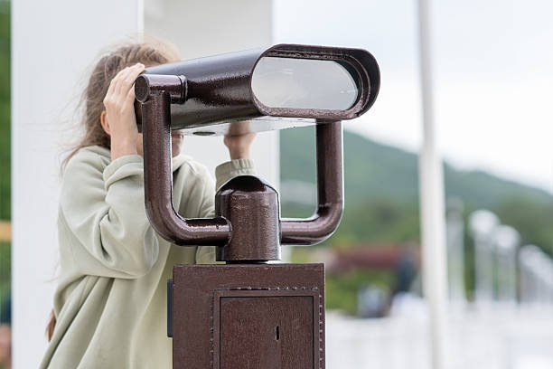 A girl looks at the mountains through a binoscope.