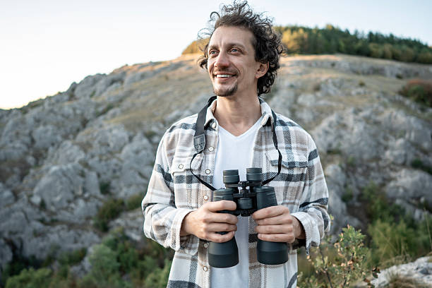 istock Smiling Man With Binoculars Outdoors Amid Rocky Hillscape On A Sunny Hiking Day With Bright Scenery 2237764128