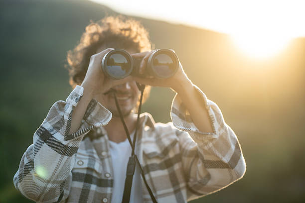 istock Young Man Outdoors Using Binoculars at Sunset in Plaid Shirt, Exploring Nature 2237765290