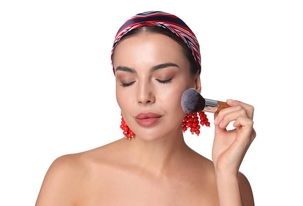 Beautiful woman applying makeup with brush on white background