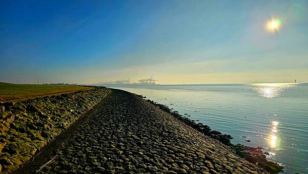 istock Sunny Coastal Walkway on a Dike Overlooking the River Estuary and Container Port. (Focus on location and elements) 2237767477