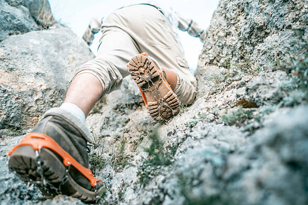 A determined climber tackles a rugged rock ascent, using sturdy orange-strapped boots for grip. Outdoor adventure atmosphere, emphasizing endurance, focus, and safety during mountain hiking.