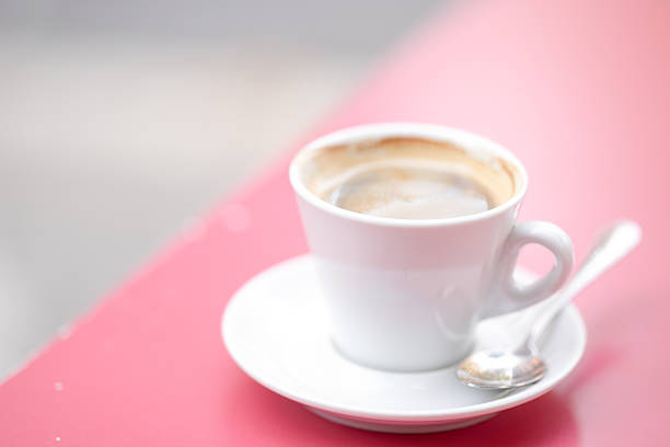 A white coffee cup sits on a red table with a spoon next to it. The cup is half full, and the spoon is resting on the edge of the cup. Concept of relaxation and comfort