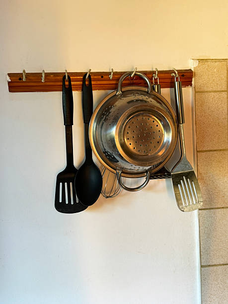 Stock photo shows a kitchen equipment neatly hanging on a rail, including a spatula, whisk, plastic spoon, and colander. This organized setup highlights functional cooking tools, efficient kitchen storage, and a clean culinary workspace