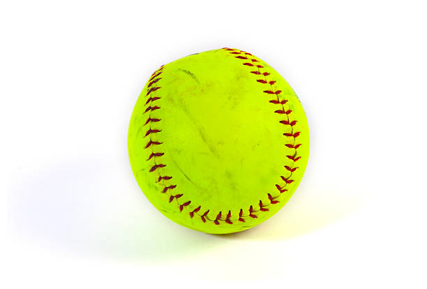 A used, optic yellow softball with red stitches, isolated on a white background. The scuff marks on the ball show signs of gameplay and competition in this popular sport.