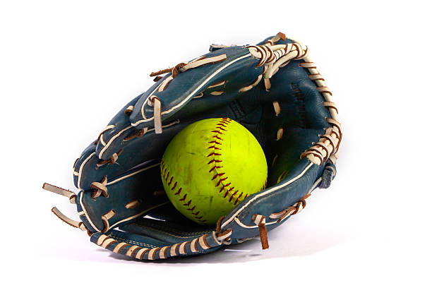 Studio shot of an old baseball resting on top of a catcher's mitt on grass with black background.