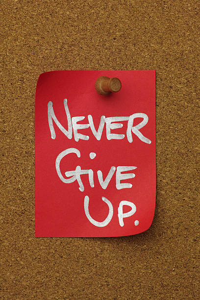 istock Red paper note pinned to a cork message board, with the short phrase 'NEVER GIVE UP.' written on it. 2237810846