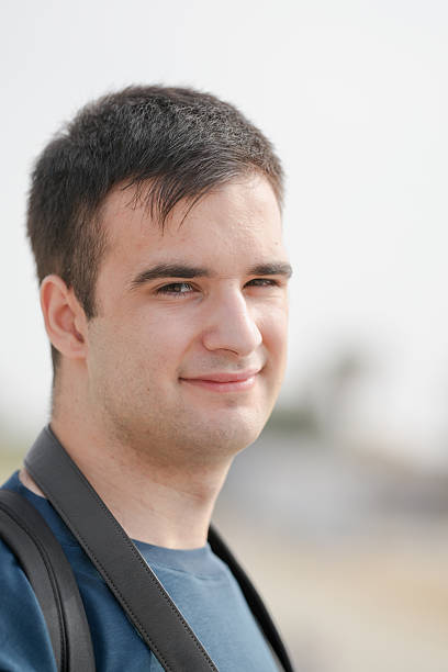 A man with a black backpack and a blue shirt is smiling. He has a beard and a shaved head