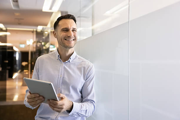 istock Businessman stands in office hallway, smiling while holds digital tablet 2237814875