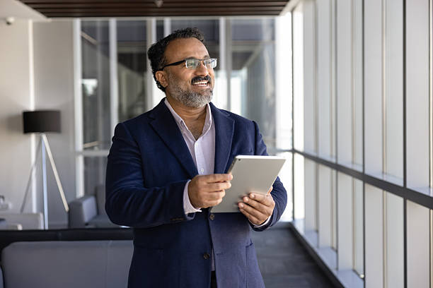 istock Older successful Indian businessman holding tablet, looking out window 2237817950