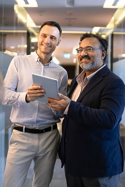 istock Two businessmen stand in modern office hallway with tablet 2237819975