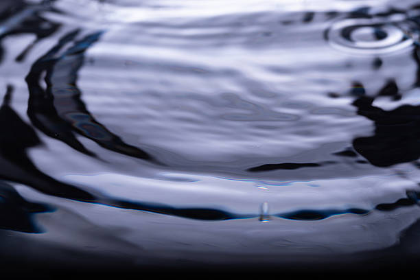 358.Close-up of water surface with concentric ripples from central impact. Blue and black reflections create glossy, abstract texture. Fluid motion and symmetry enhance visual depth.