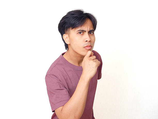 Thoughtful young Asian man touching his chin with curious expression, isolated on white background, concept of thinking, decision making, or advertisement idea.