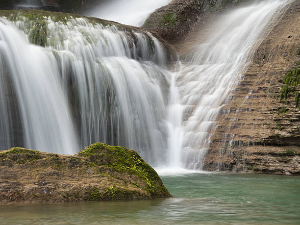 Close-up of Waterfall Cascading Down Rocks - Vertical shot using long exposure to create a silky, smooth effect of water rushing over textured, reddish-brown rock formations into a pool.