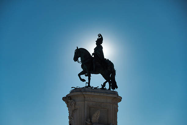 istock King Jose I Statue Silhouetted Sunburst - Dramatic low-angle silhouette of the bronze equestrian statue of King Jose I in Lisbon's Praça do Comércio, featuring a striking sunburst against a bright blue sky. 2237839881