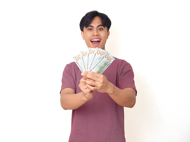 istock Excited young man smiling while holding cash money in hand with surprised expression, isolated on plain background, perfect for finance, business, and success concepts. 2237839927