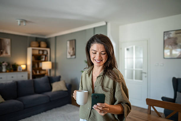 istock Woman smiling using smartphone and drinking coffee at home 2237841019