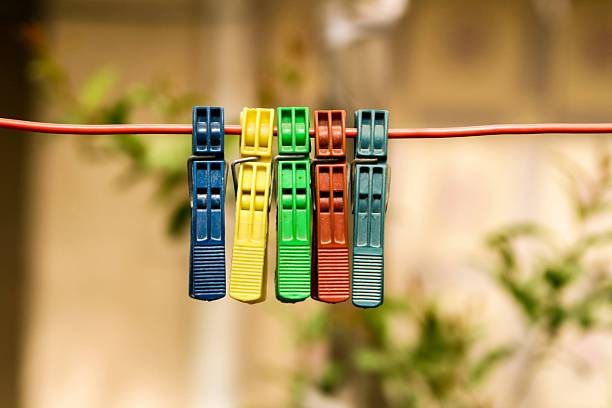 Colorful clothespins on a red line in a blurred outdoor setting, showcasing vibrant colors and simplicity.