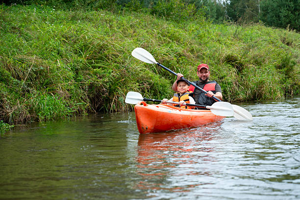 Smiling father and son kayaking on river. Family enjoying aquatic sport against mountain. They are happy during vacation.