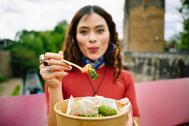 Woman holding takeaway lunch up towards camera, front view, focus on foreground