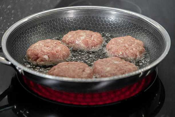 Detailed view of five fresh cutlets frying in hot bubbling oil within a textured non-stick pan, highlighting home meal preparation on a modern induction cooktop